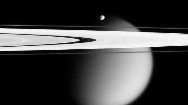 Vista de Epimeteo, luna menor de Saturno, sobre los anillos. Al fondo, Titán