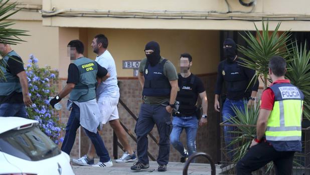 Policías y guardias civiles se llevan a uno de los detenidos tras un registro.